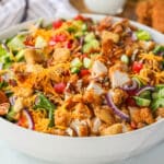 A white bowl of chicken tender salad with cheddar cheese and red onion