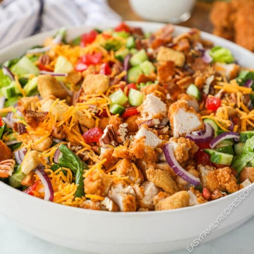 A white bowl of chicken tender salad with cheddar cheese and red onion