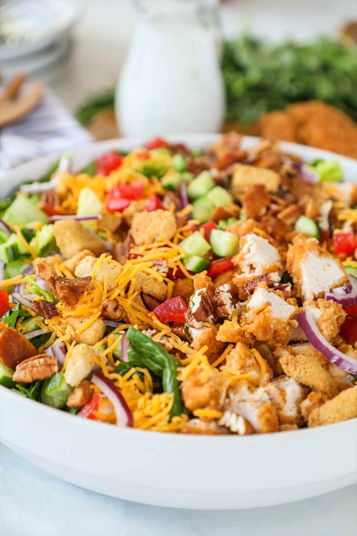 A white bowl full of chicken tender salad with a drizzle of ranch dressing and a bottle of dressing in the background.
