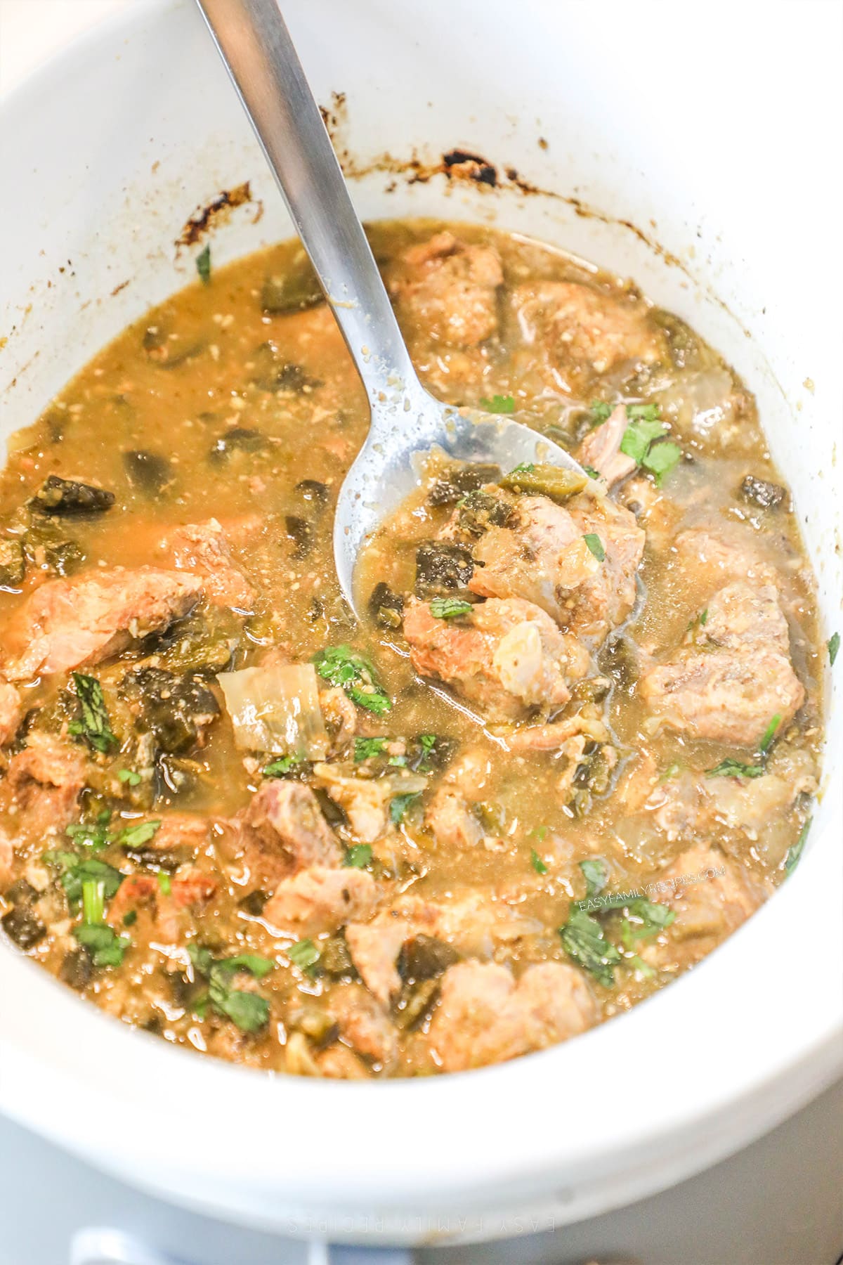 A spoon scoops out a serving of Crockpot Pork Chile Verde from the slow cooker