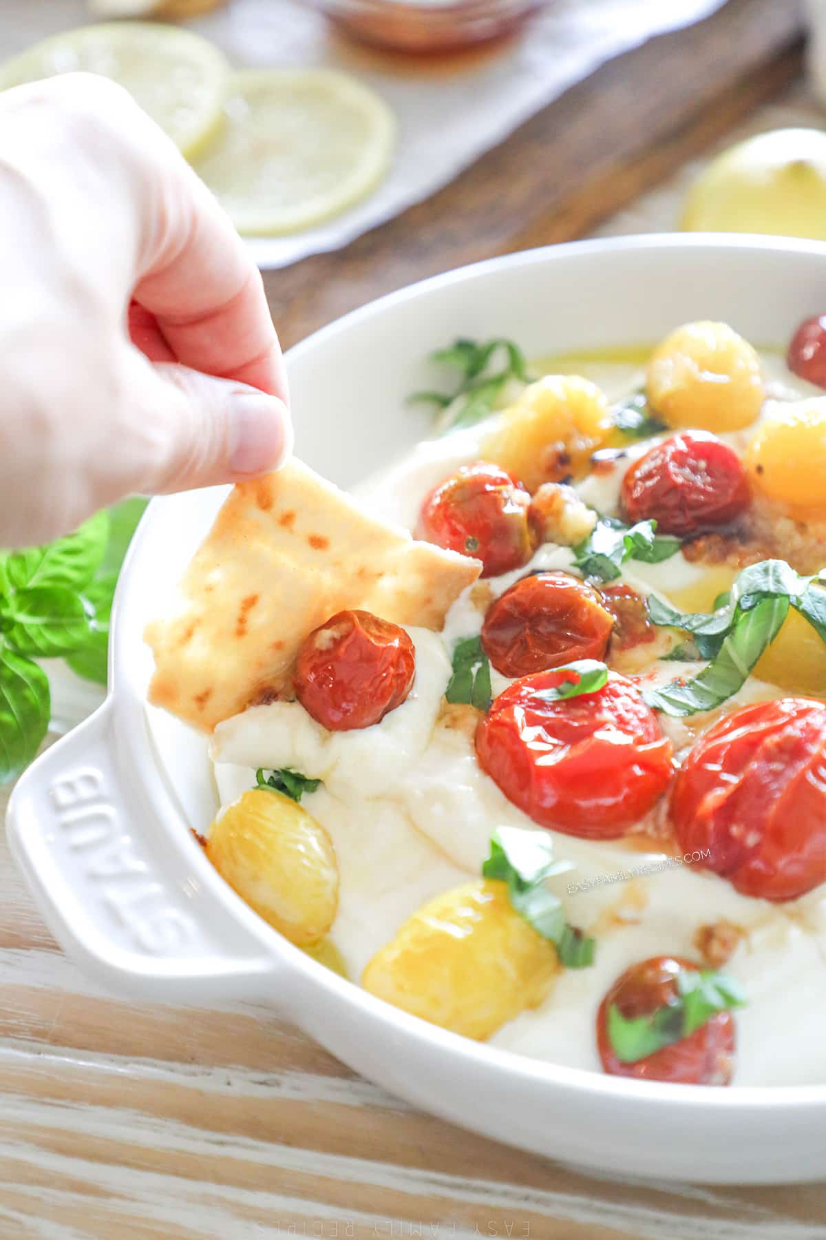 a piece of pita bread being dipped into a dish of whipped honey feta topped with roasted tomatoes.
