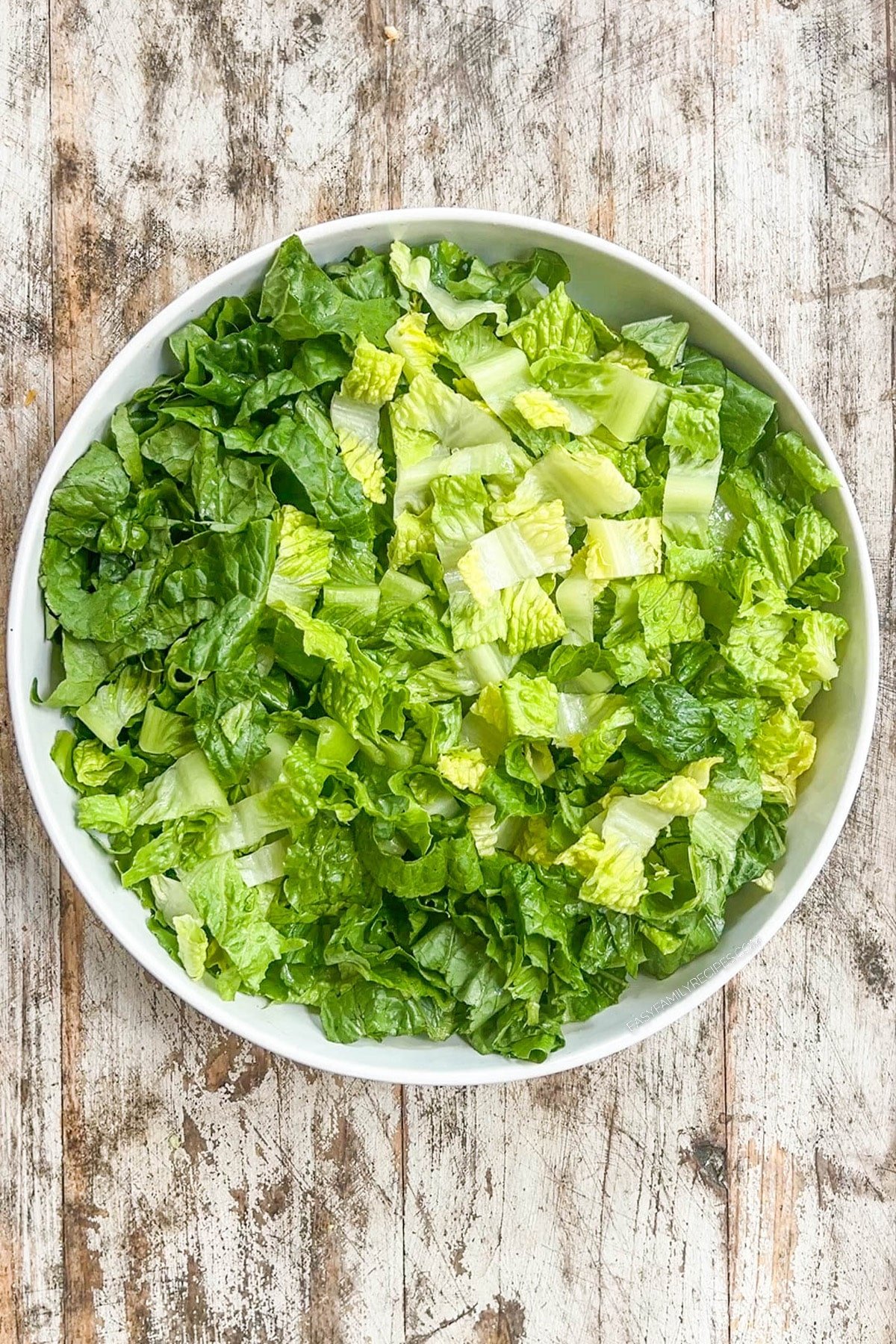 Step one for making chicken tender salad; add the romaine lettuce to the bowl.