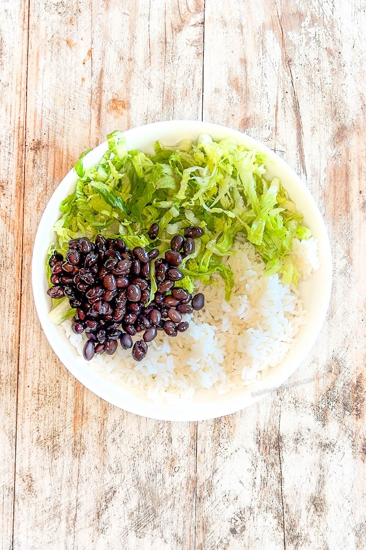 Step 2 for making Honey BBQ chicken bowls - add lettuce, beans, and rice to the bowl. The text reads, "Honey BBQ Chicken Bowl"