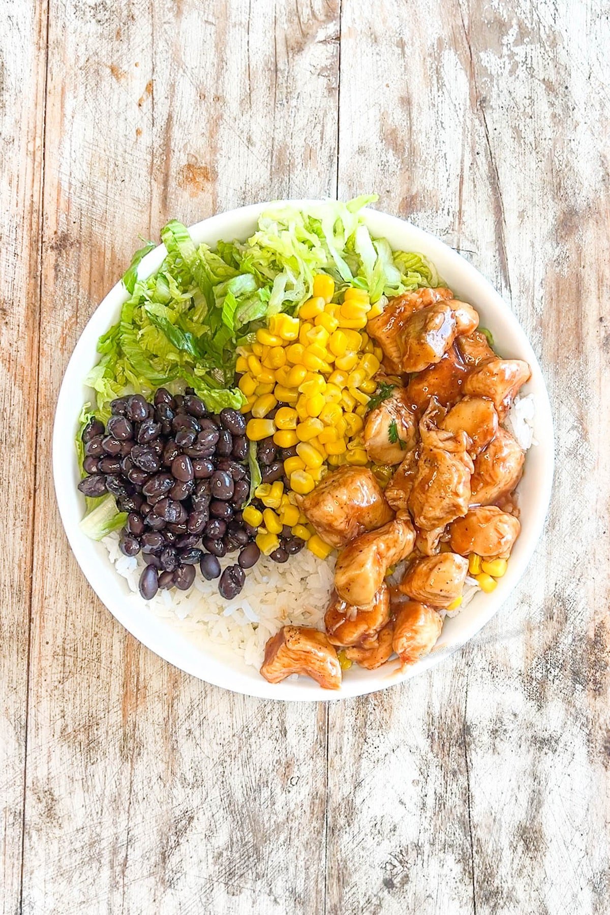 Step 3 for making honey BBQ chicken bowls - add honey BBQ chicken to the bowls.