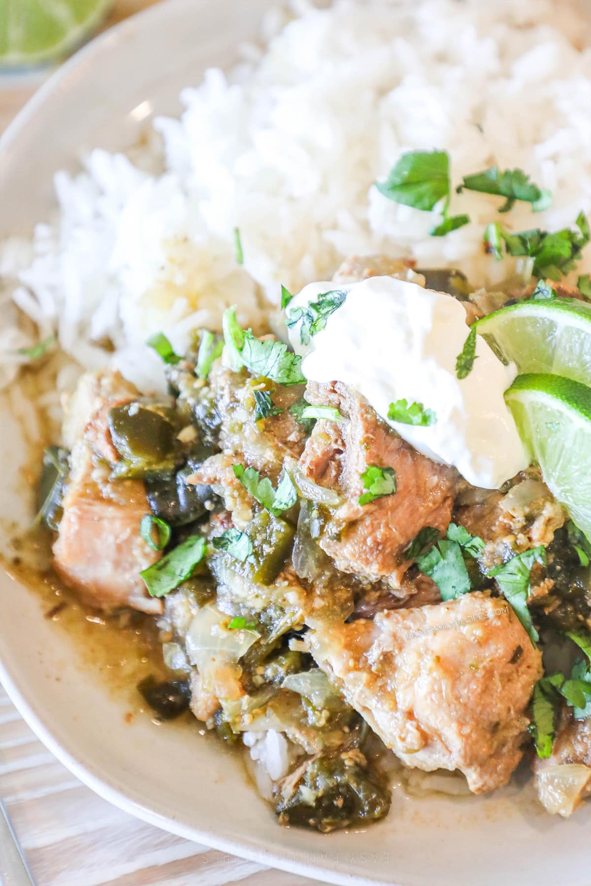 A serving of Crockpot Pork Chile Verde on a white plate with sour cream, cilantro, and a side of rice.