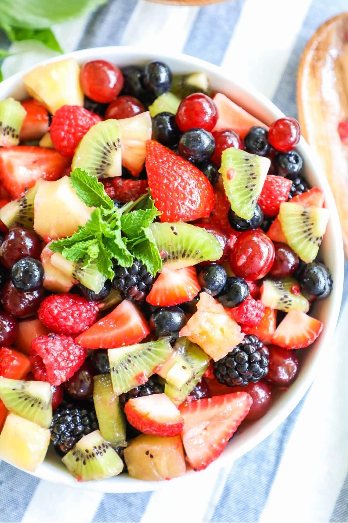 a bowl of fruit salad - strawberries, blueberries, kiwi, blackberries, and a spring of mint