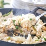 A spoon scoops the cheesy chicken for Chicken Cheesesteaks from the cast iron skillet.