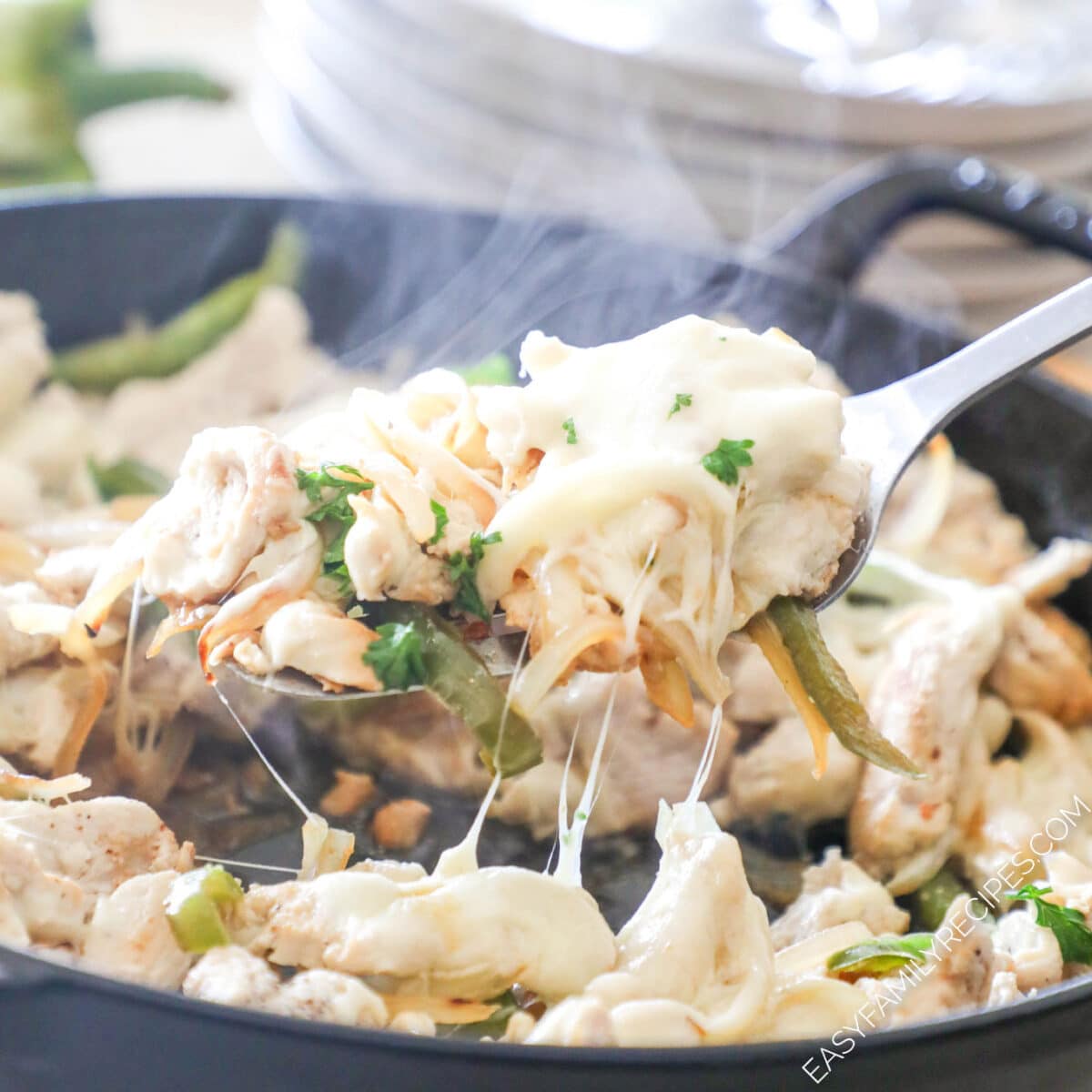 A spoon scoops the cheesy chicken for Chicken Cheesesteaks from the cast iron skillet.