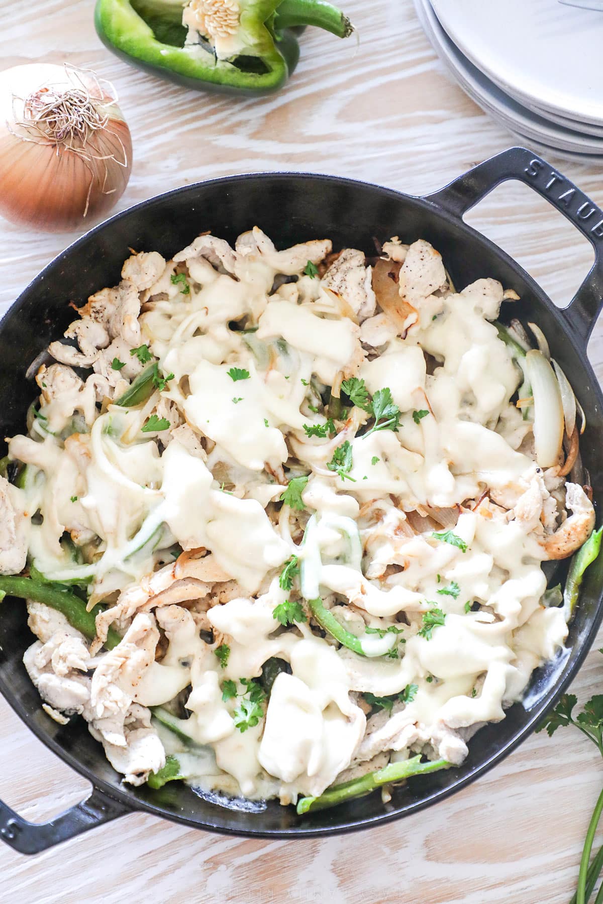 Chicken for Chicken Cheesesteaks is sauteed in a skillet. The skillet sits on a whitewashed wood background. 