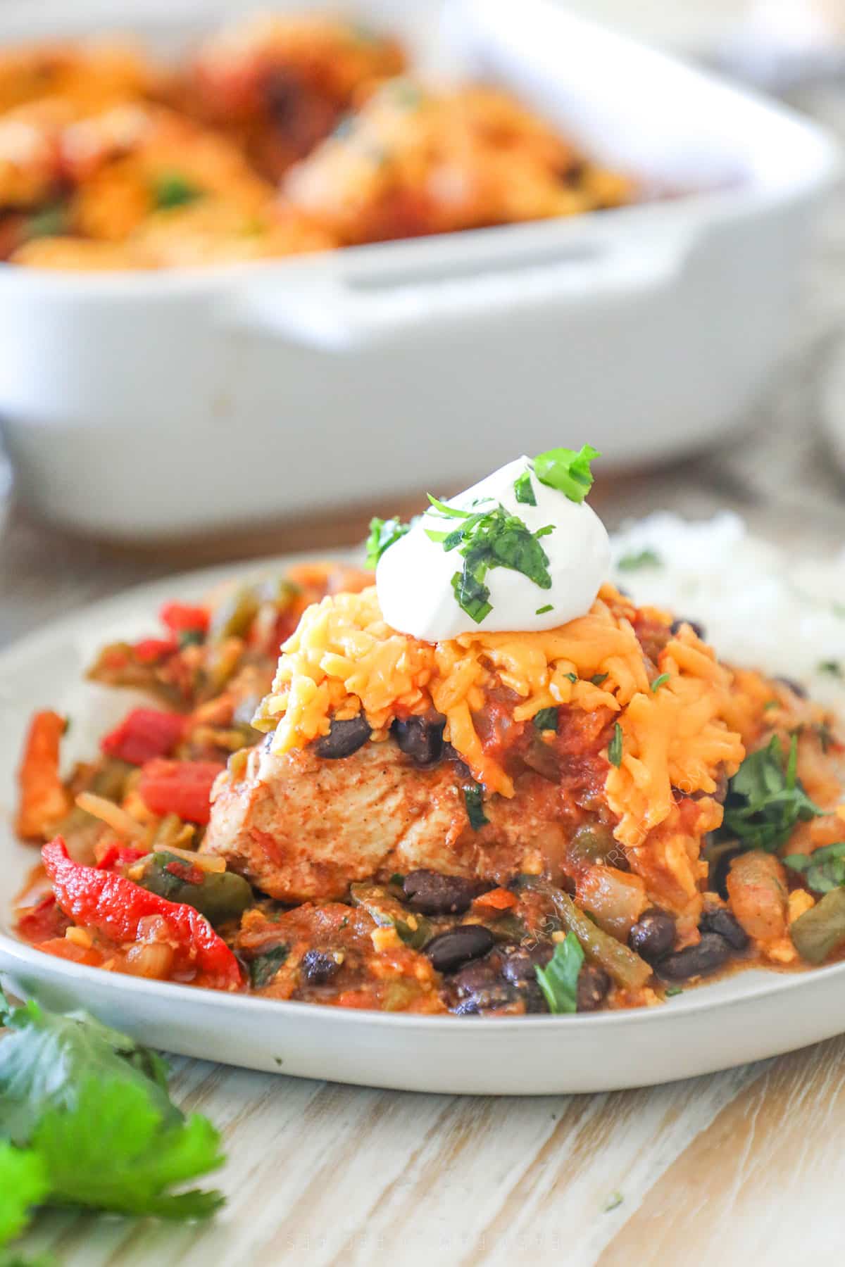 A serving of Mexican Chicken Bake with sour cream on a white plate.