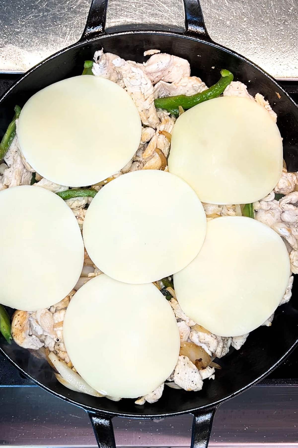Step 4 for making chicken cheesesteak sandwiches: add the cheese over the top
