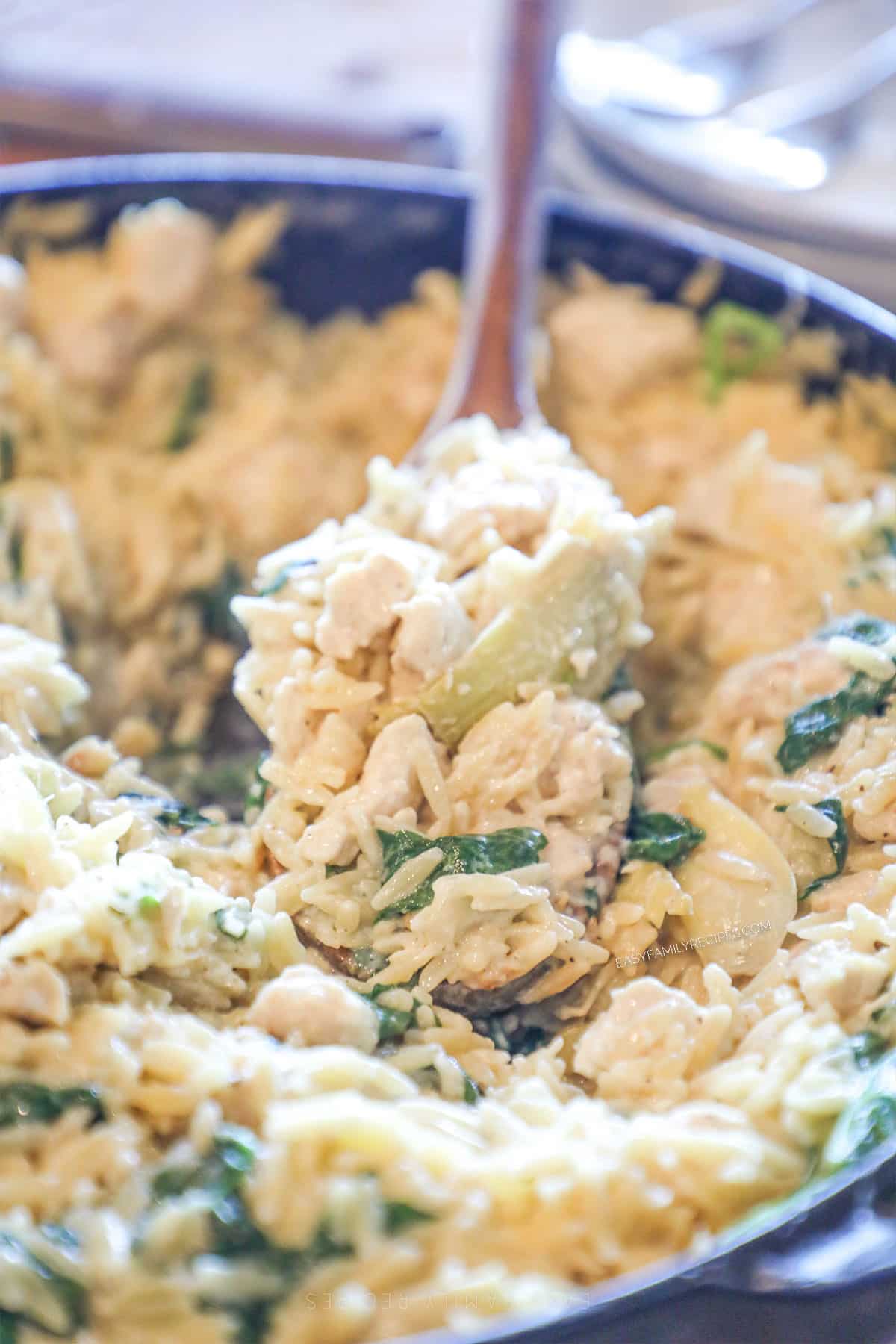One pot spinach artichoke chicken orzo with a spoon lifting some up.