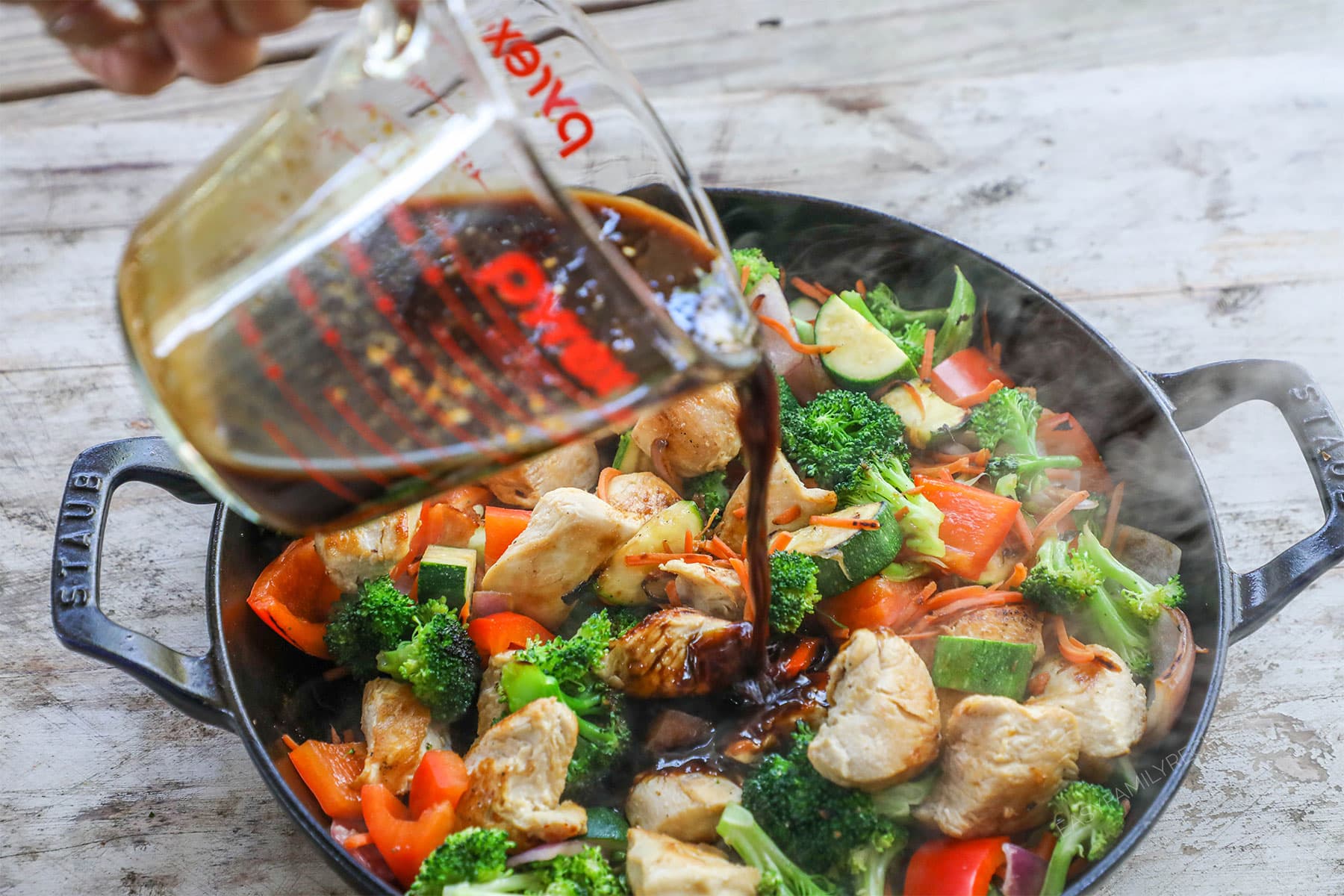 Pouring stir fry sauce into chicken and vegetables to prepare dinner.
