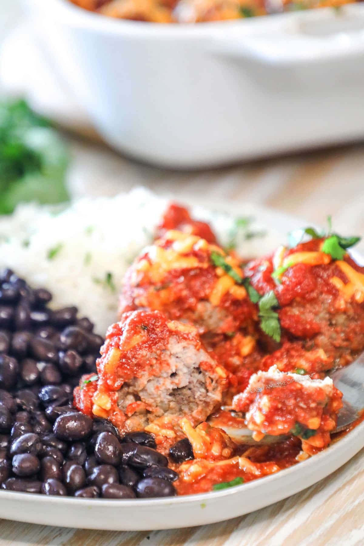 A serving of chili cheese meatballs on a white plate with black beans and rice