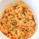 Crockpot Bourbon Chicken in a crock with sliced scallion garnish.