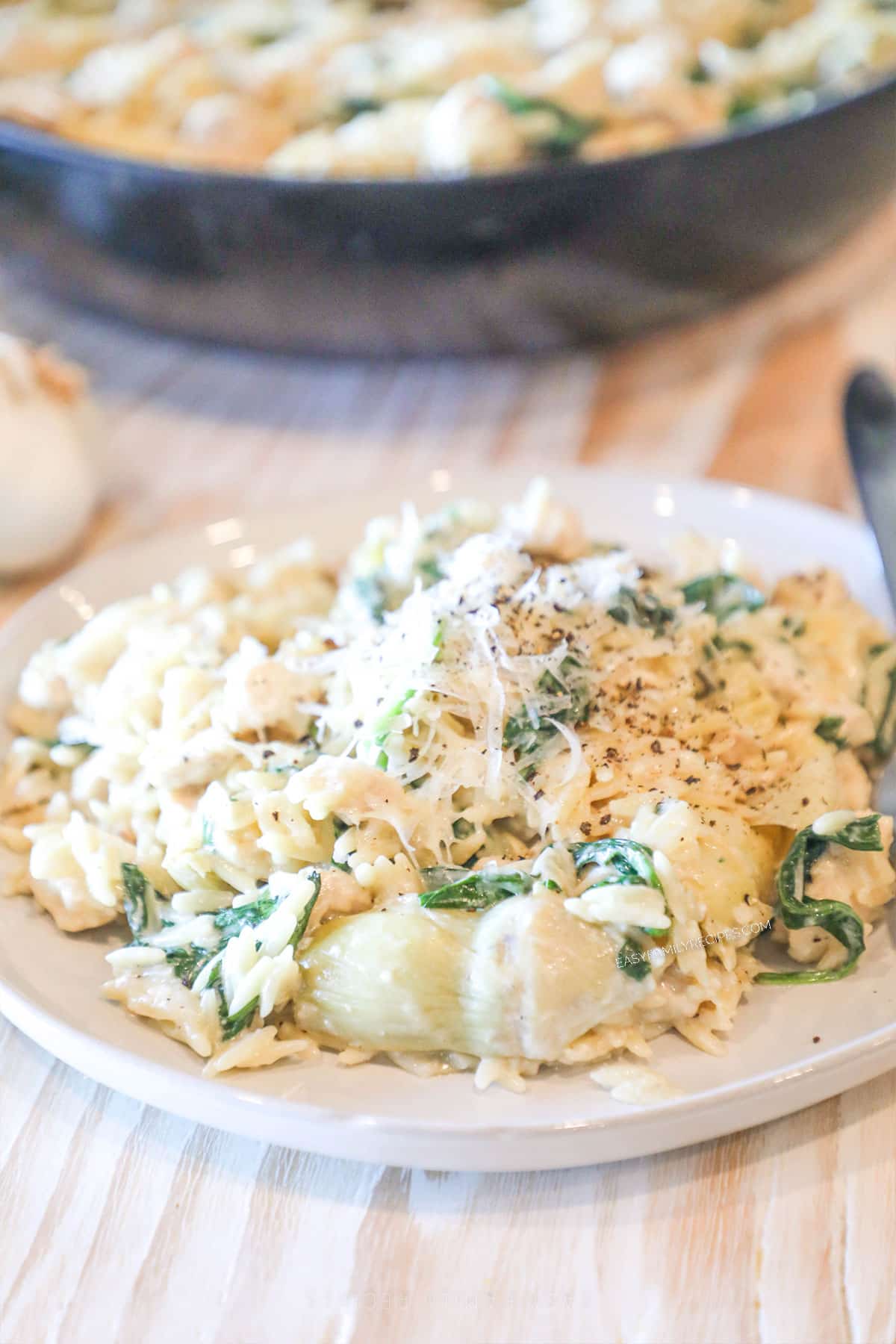 Serving of spinach artichoke chicken orzo on a plate with pan nearby.