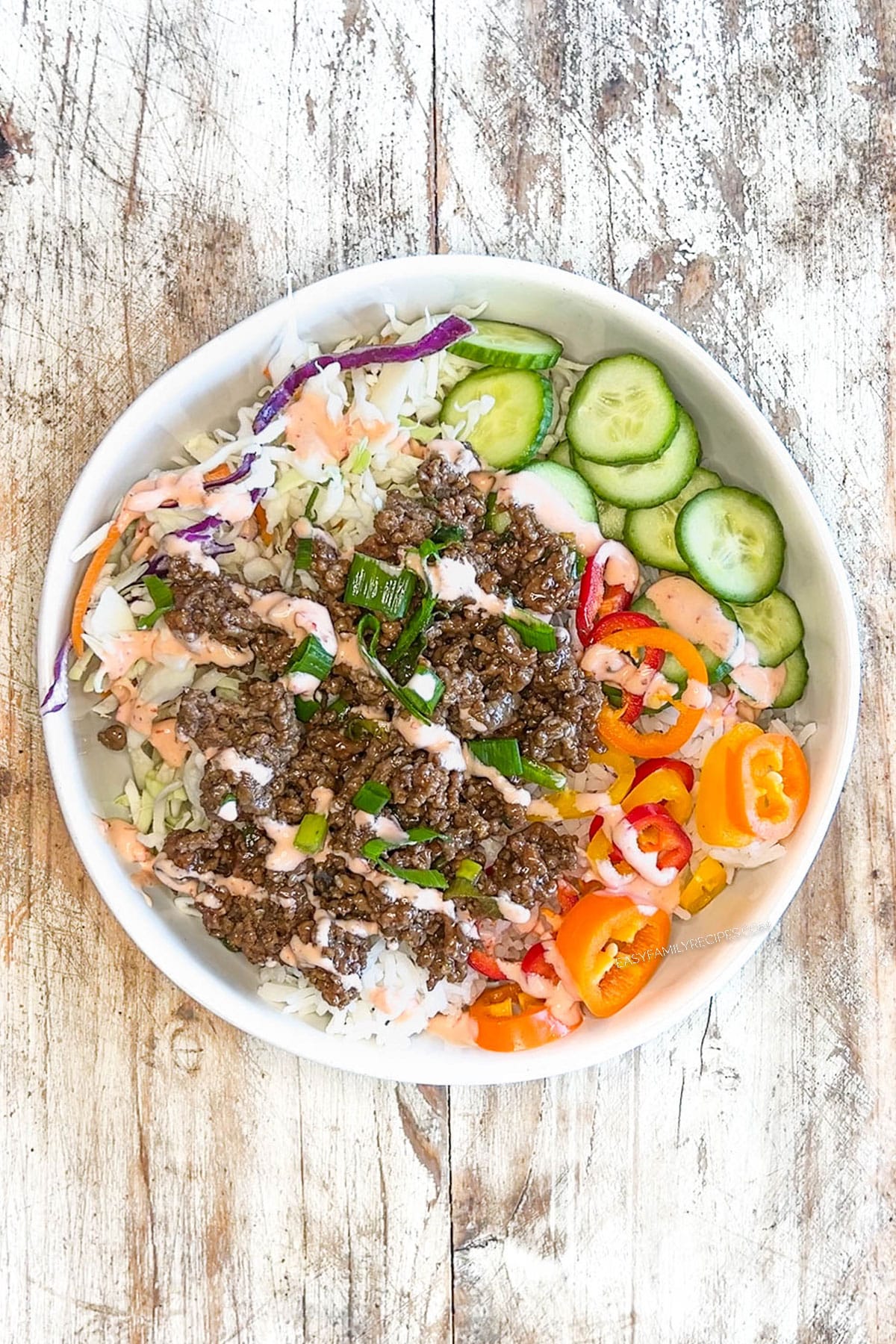 above image of an assembled beef bulgogi bowl topped with creamy chili sauce.