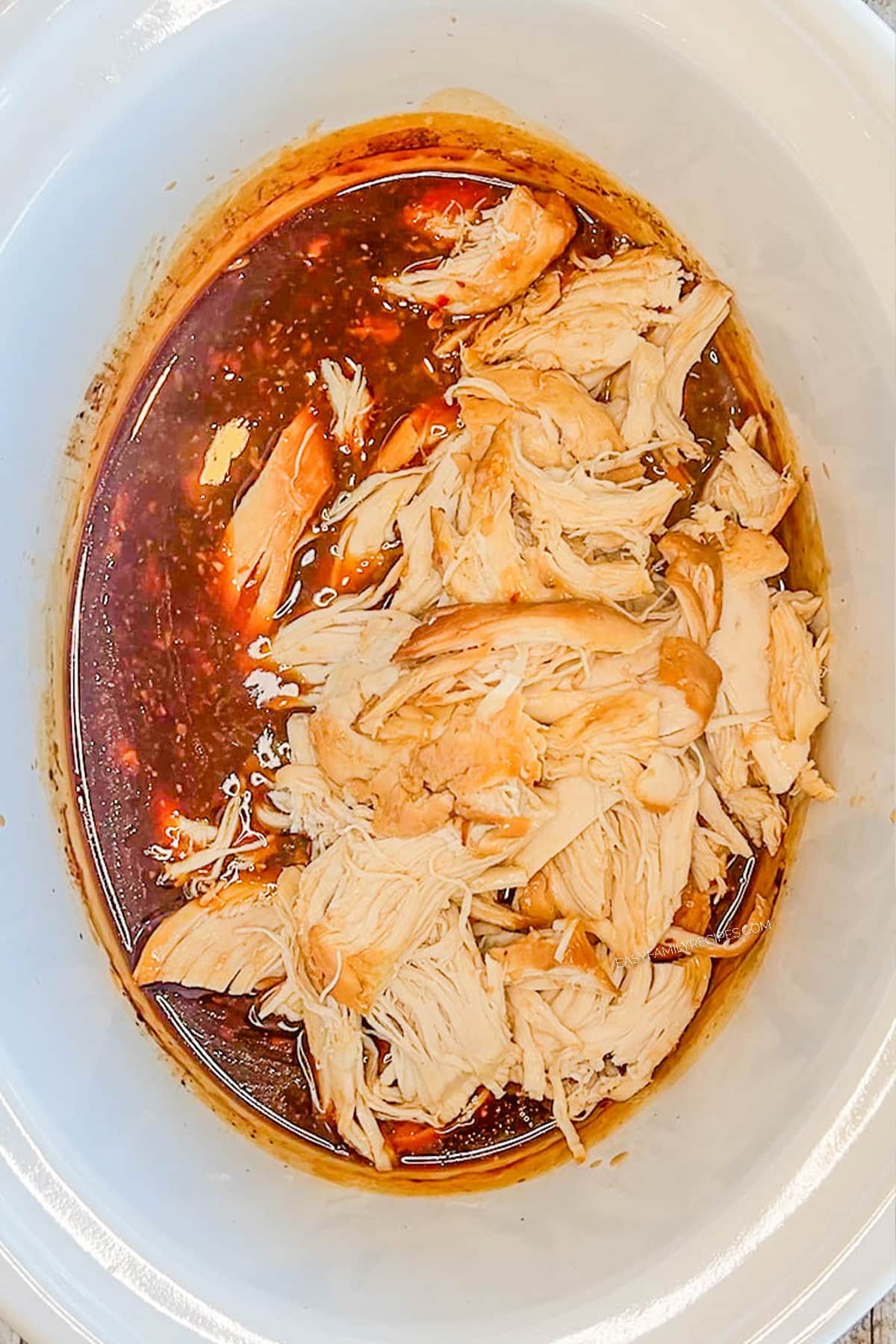 Step 5 for how to make bourbon chicken: Shred the chicken in the Crock Pot.