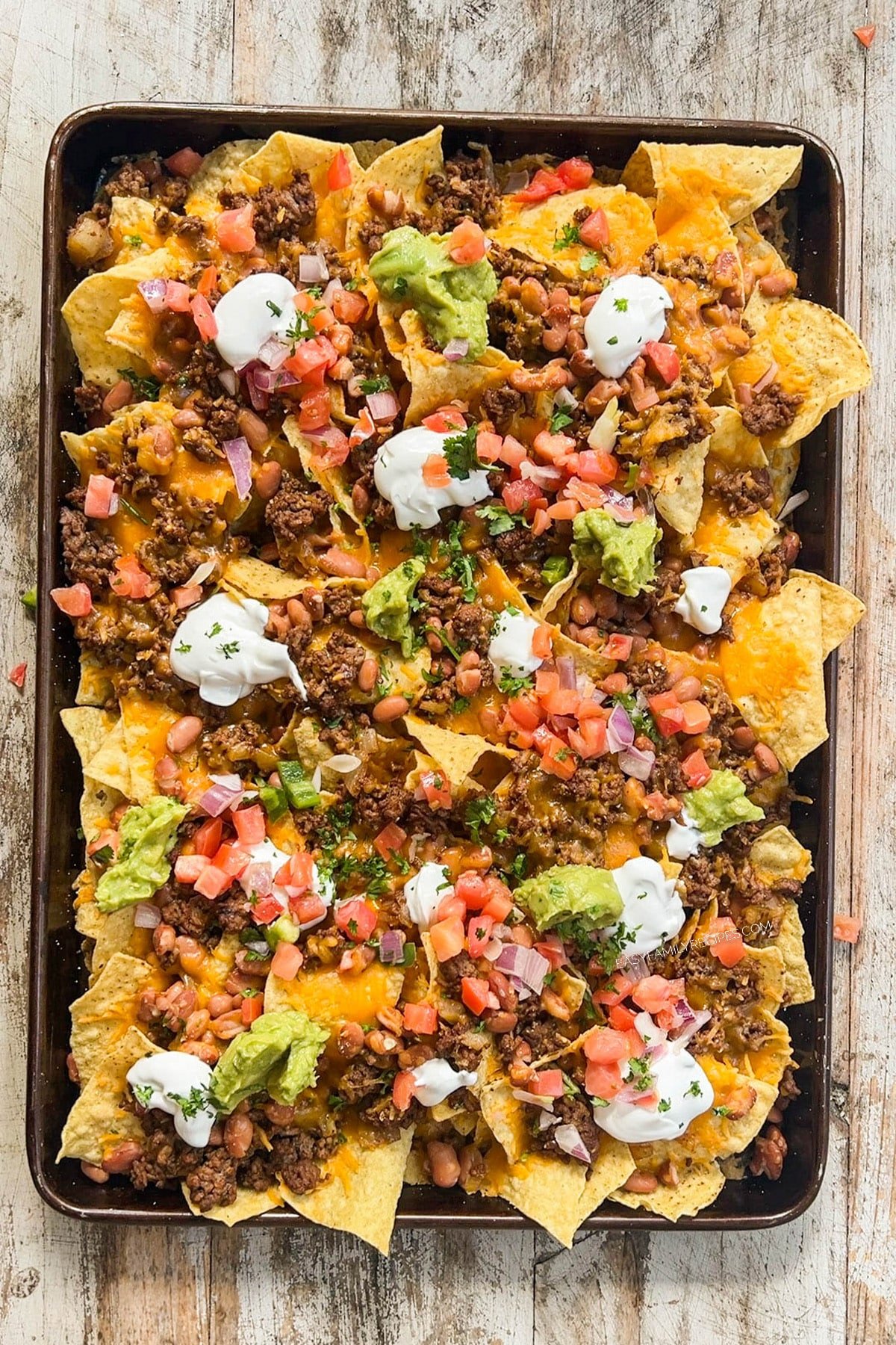 above image of ground beef nachos on a sheet pan.