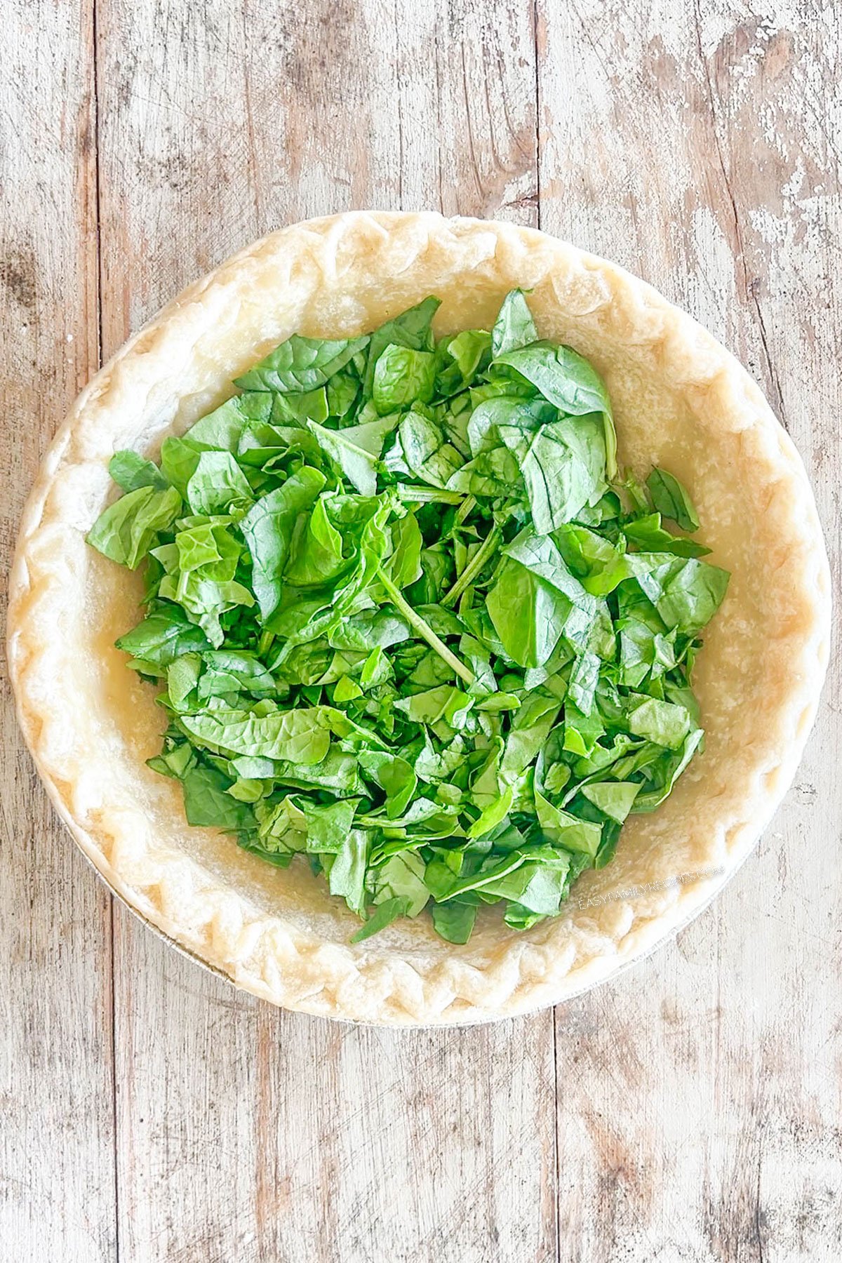 Step 2 for how to make Marry Me Chicken Quiche - layer the spinach on the bottom of the pie crust.