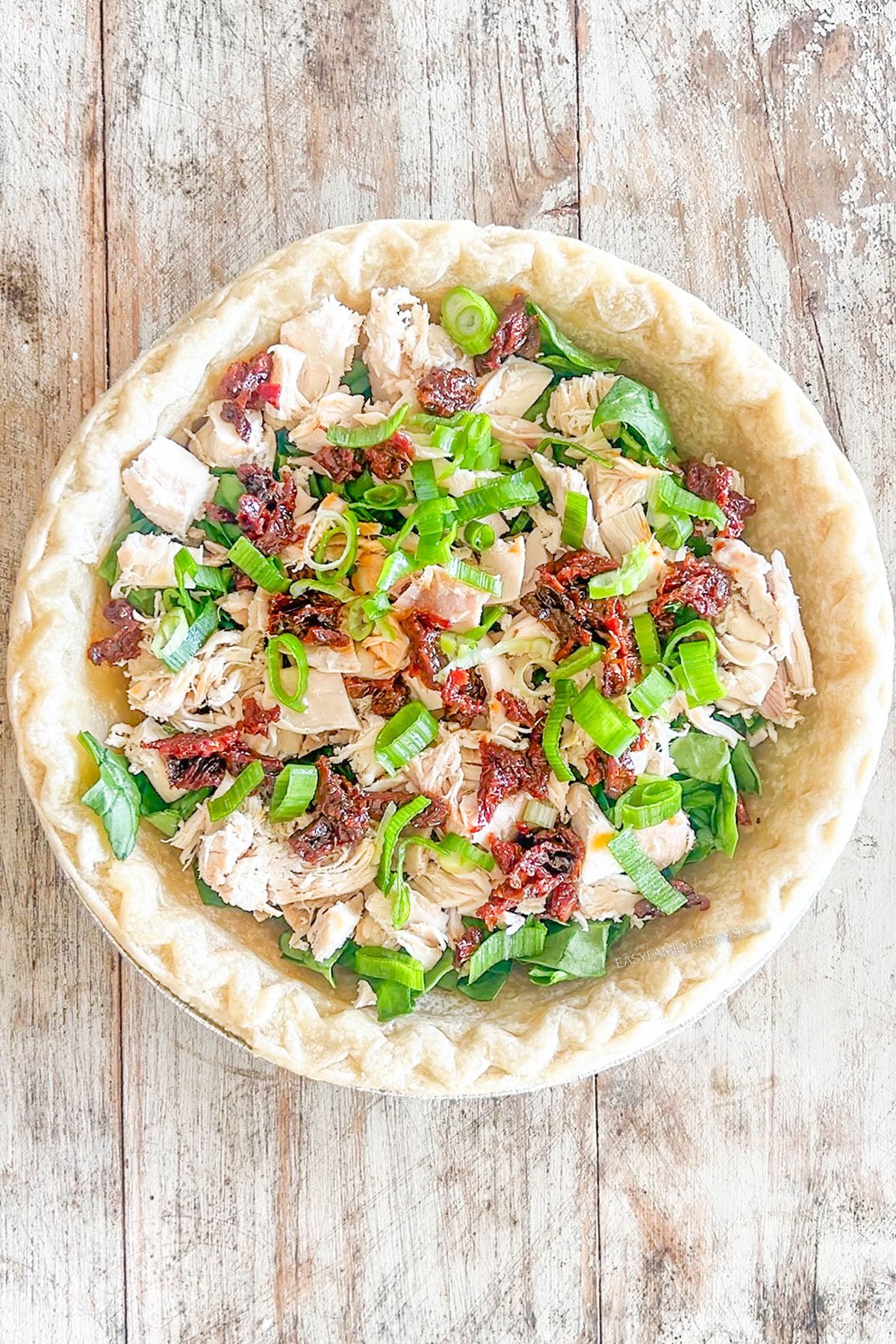 Step 3 for how to make Marry Me Chicken Quiche - add the chicken, sun-dried tomatoes, and green onions, on top of the spinach.