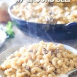A white plate full of loaded mac and cheese with grond beef with a silver fork and a blue castiron skillet full of mac and cheese in the background. The text reads, “Ground Beef Mac & Cheese”