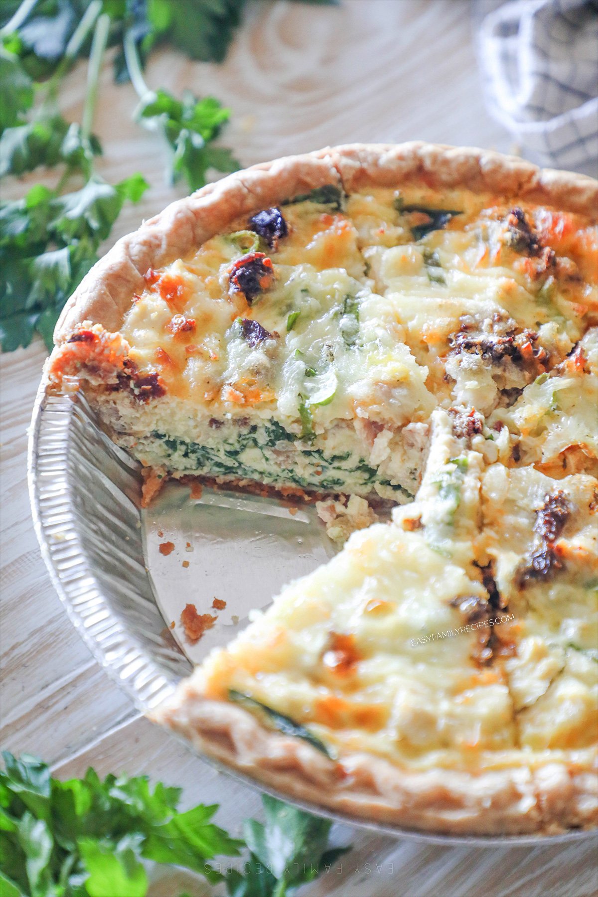Marry-me chicken quiche in a foil pie plate. A wedge has been removed. Herbs are in the background. 