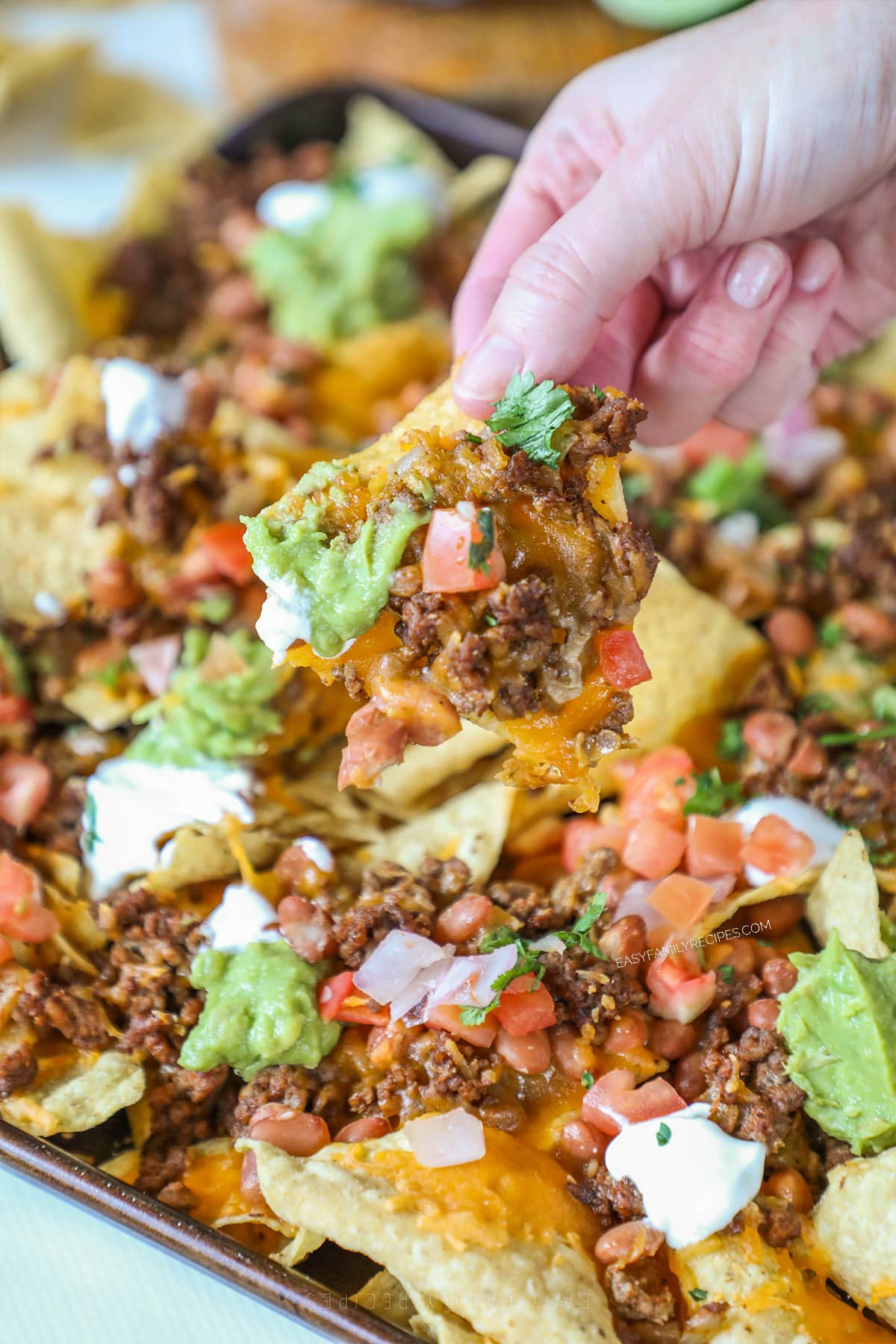 a loaded nacho being lifted off of a sheet pan of nachos.