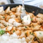 A silver fork lifts a bite of bang bang chicken out of a skillet.
