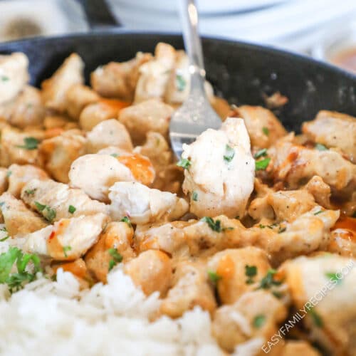 A silver fork lifts a bite of bang bang chicken out of a skillet.