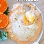 Top view of a white plate with cheesy grits and eggs along with an orange and parsley for garnish. The text reads, "Cheesy Grits with Eggs"