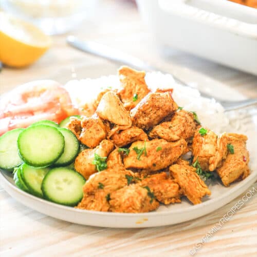 White plate full of chicken schwarma bites with cucumber.