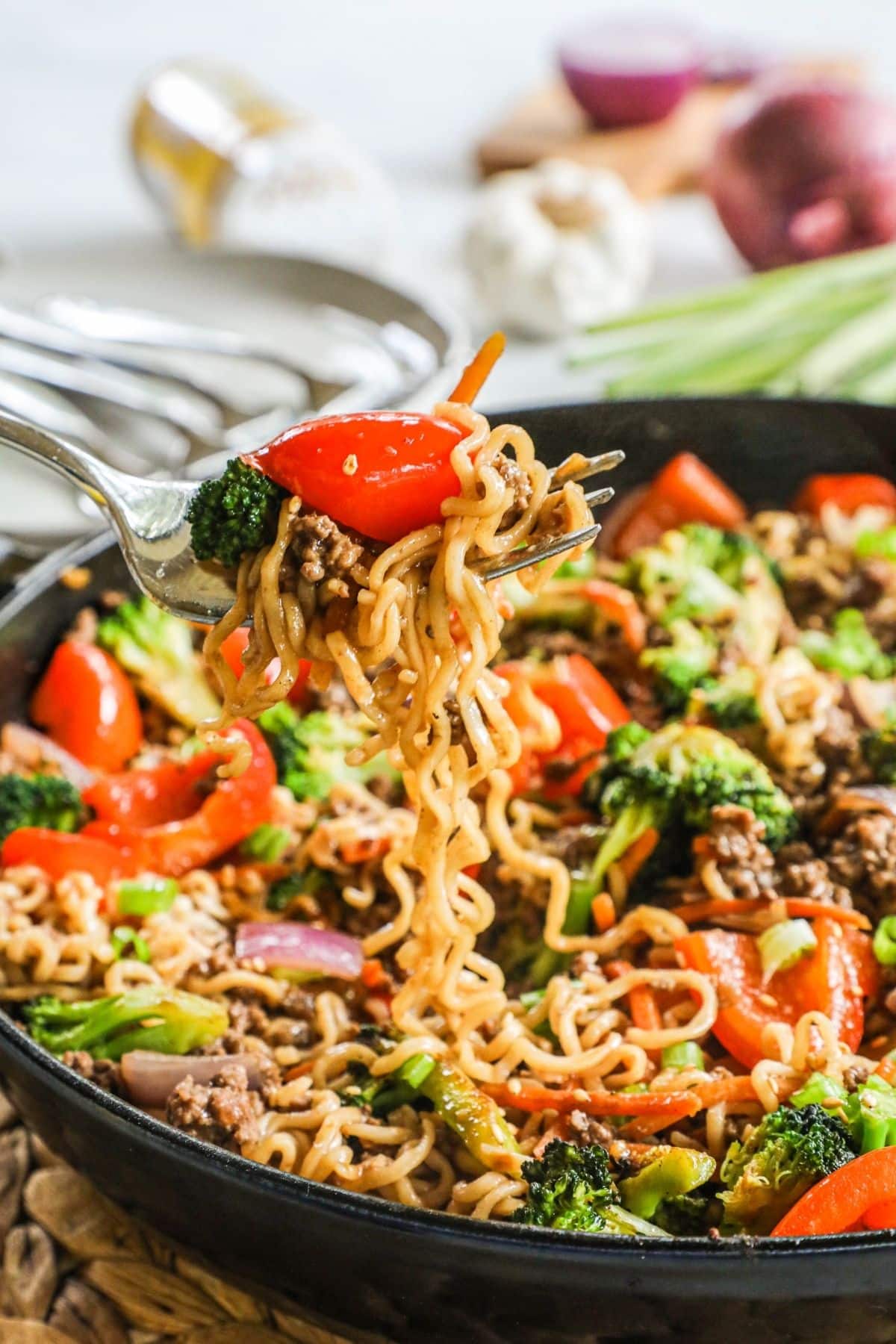 a fork lifting a scoop of beef ramen stir fry out of a cast iron skillet