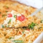 A spoon scoops out a serving of Boursin Baked Orzo in a white casserole dish.