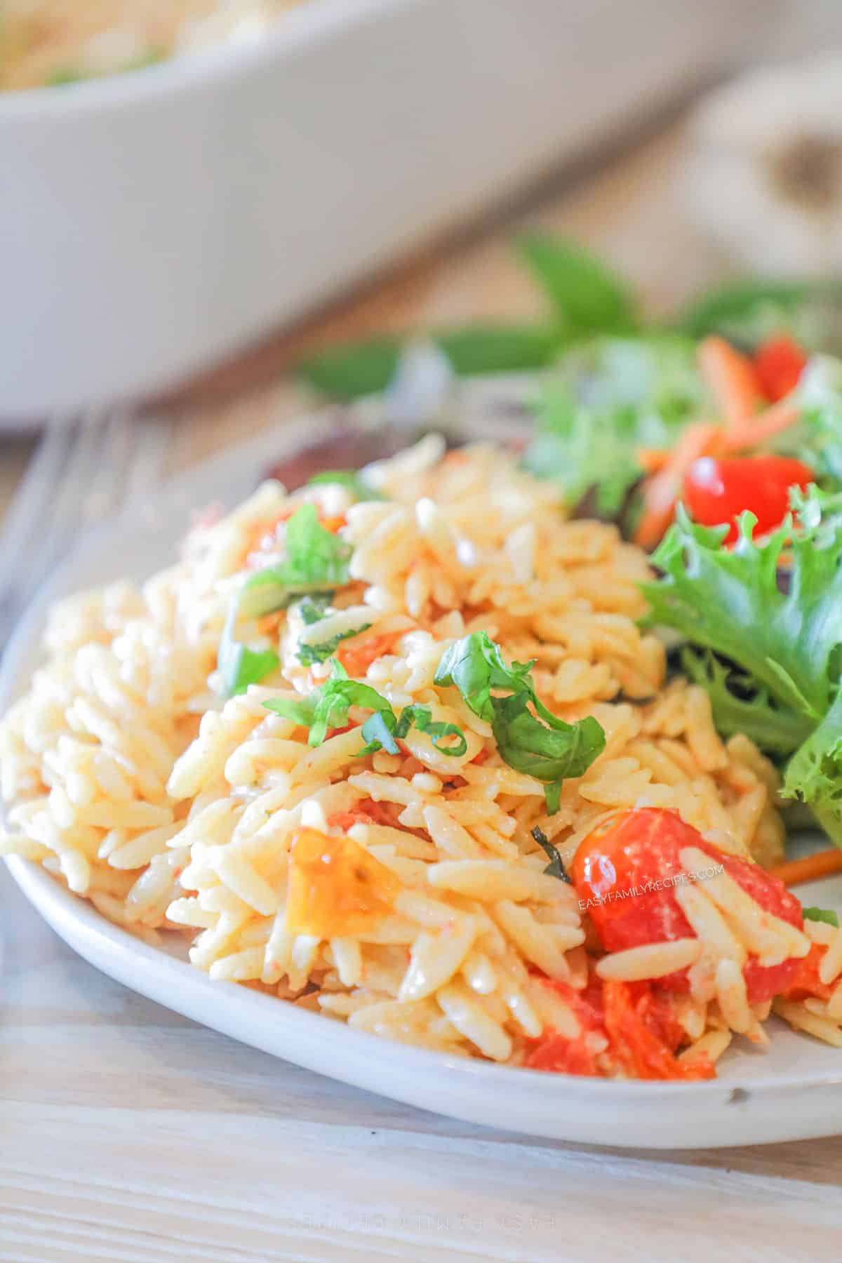 A serving of Boursin baked orzo on a white plate with a side salad.