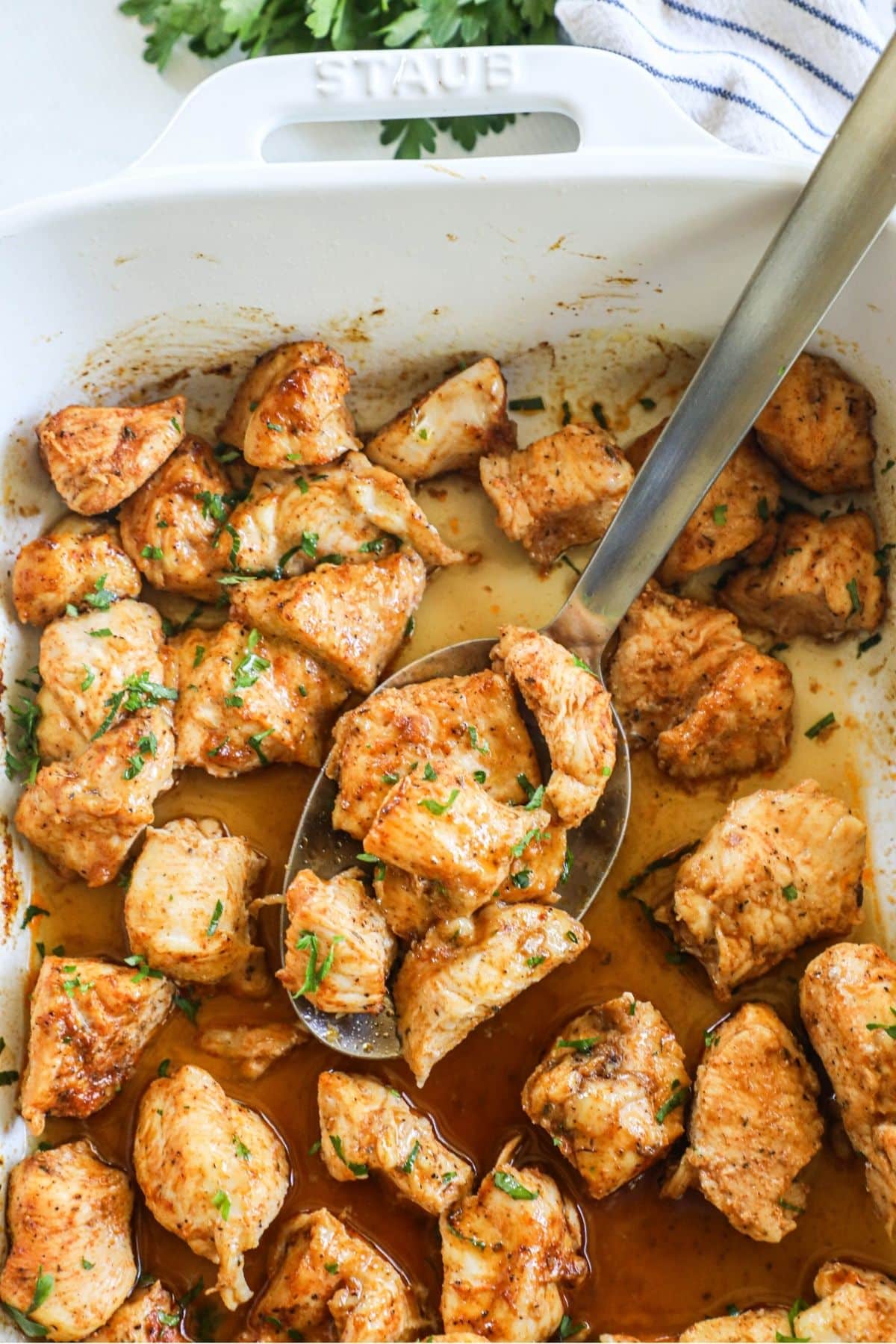 a serving spoon lifting a scoop of juicy oven baked chicken bites from a baking dish