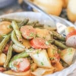A white bowl full of slow cooker sausage and potatoes with a silver fork.