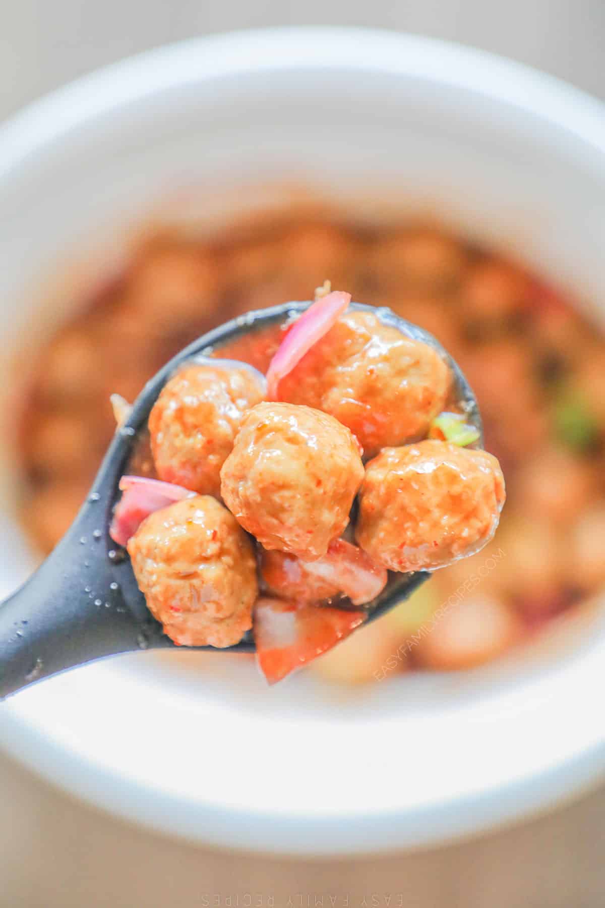A serving spoon lifts some Crockpot Sweet Chili Meatballs out of the Crock Pot.