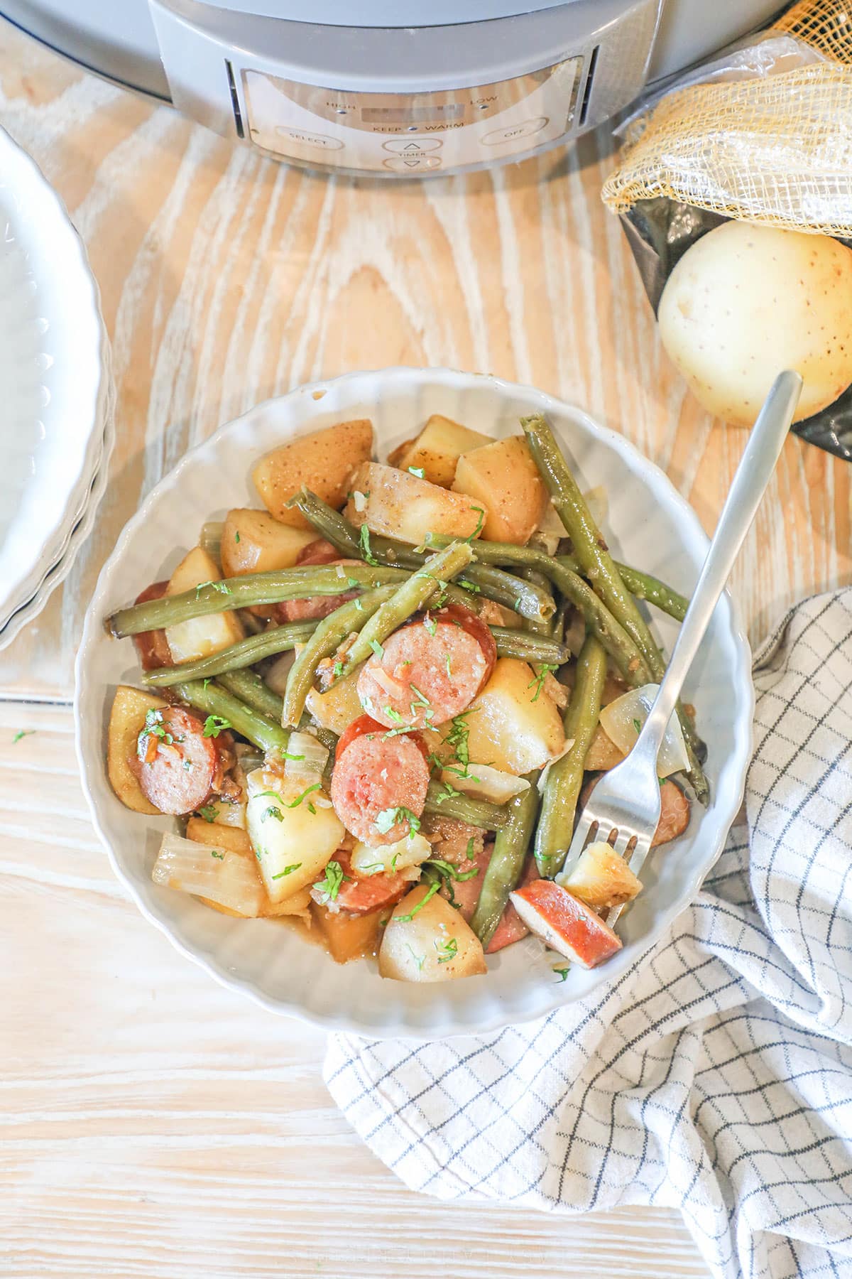 A top view of a bowl full of Crockpot Sausage and Potatoes in a white bowl with a silver fork.