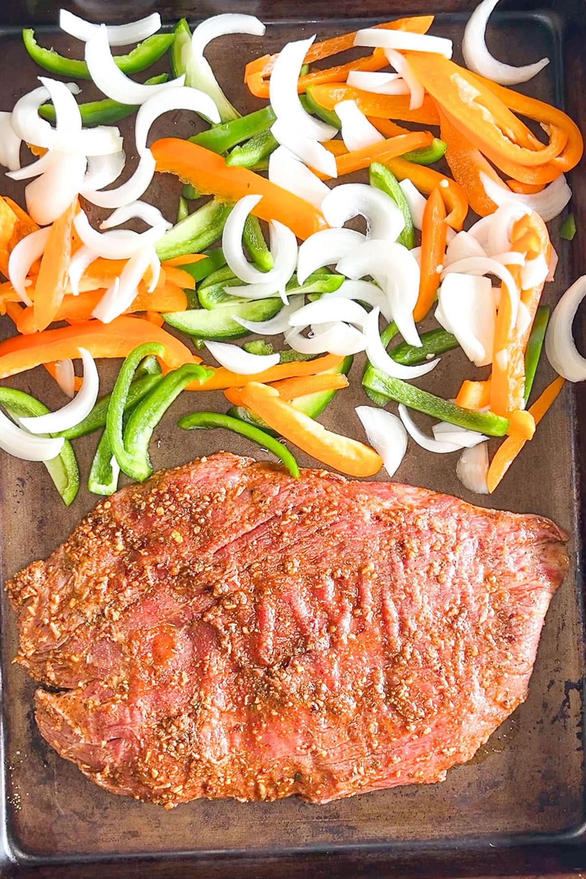Step 4 of how to make sheet pan steak fajitas: Add the veggies to the baking sheet.