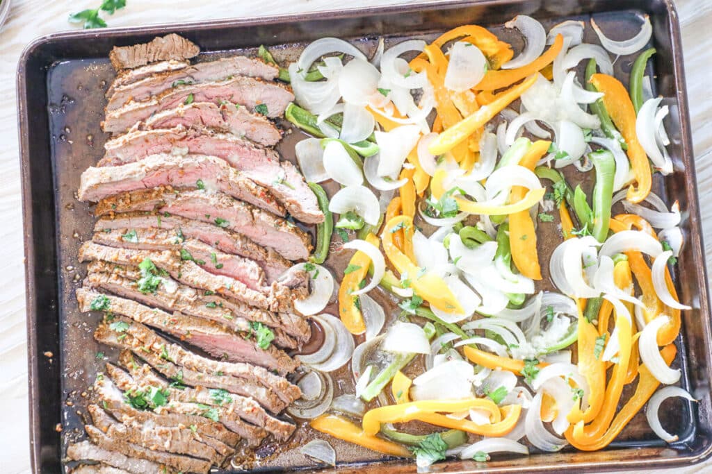 Top view of sheet pan steak fajitas on a rimmed cookie sheet.