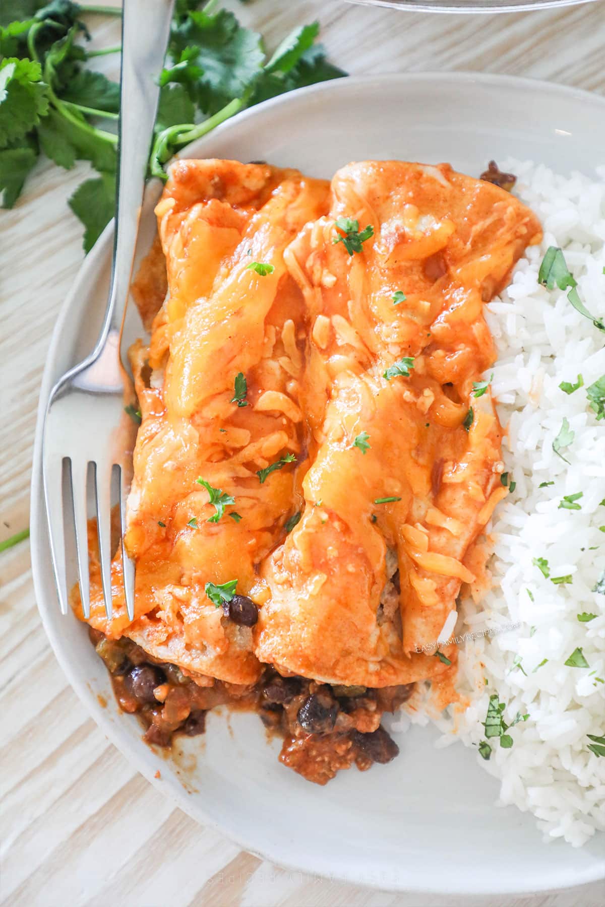two chili cheese enchiladas on a plate with a side of rice.
