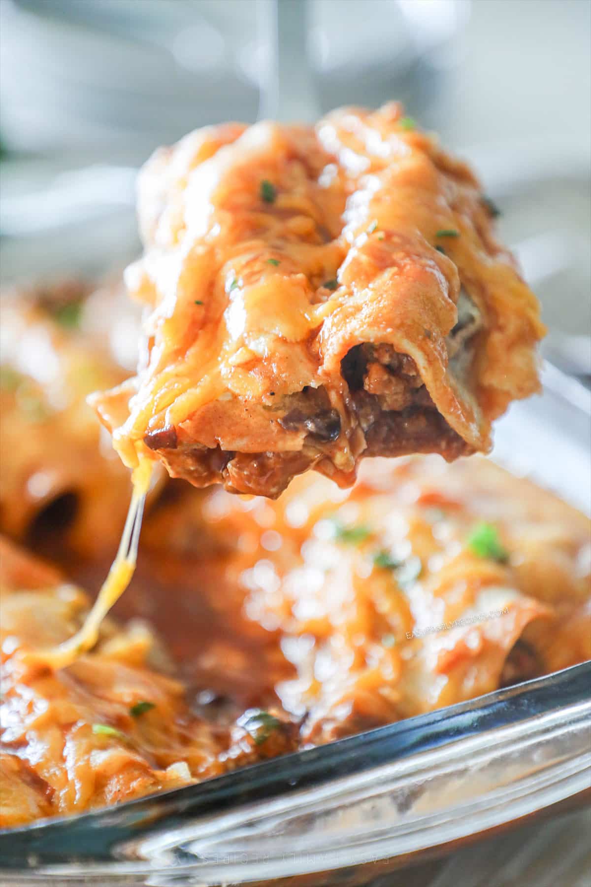 a portion of cheesy enchiladas being lifted out of a baking dish. 