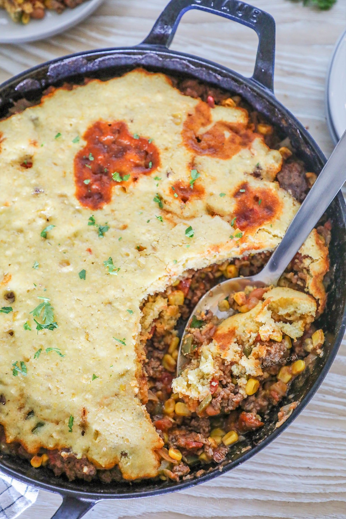 A spoon scoops out a serving of cowboy casserole from a cast-iron skillet