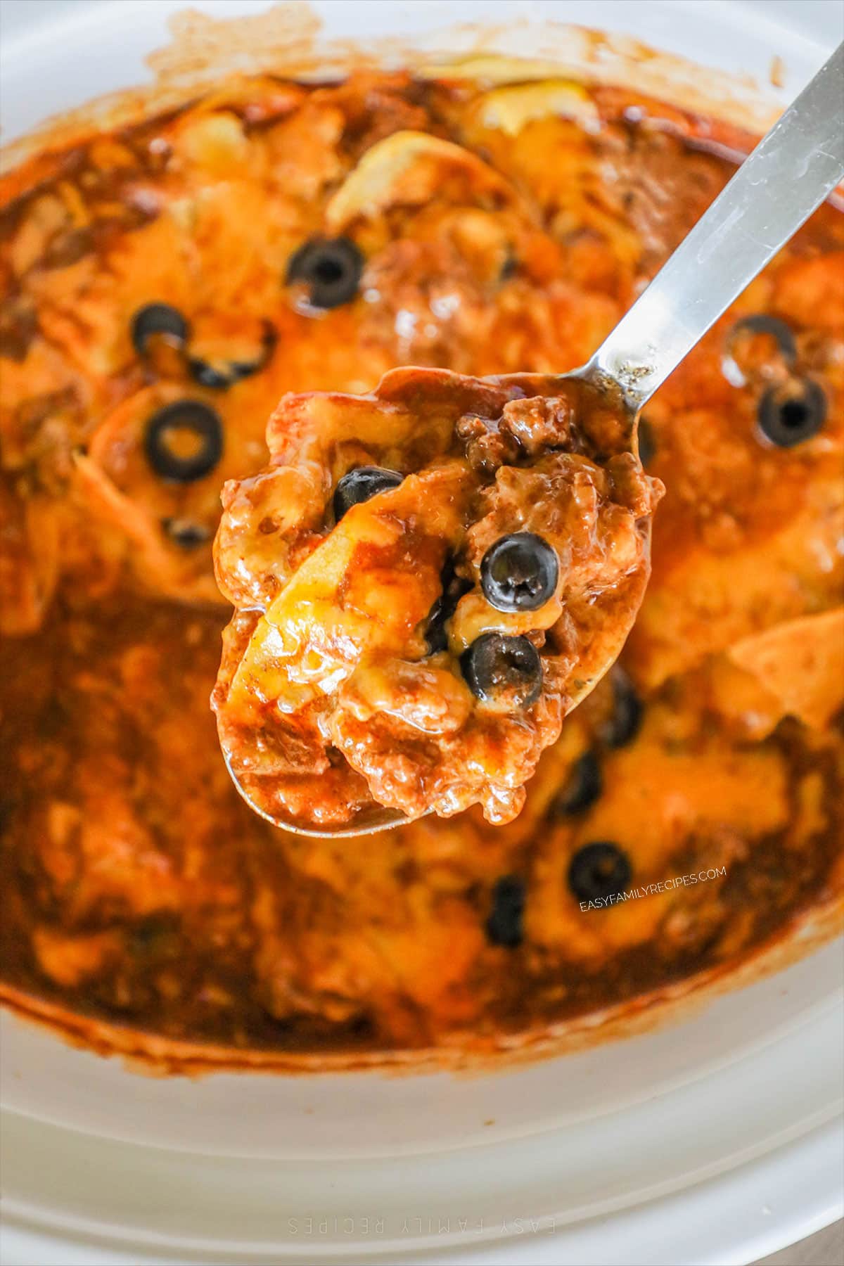 a large spoonful of enchilada casserole being lifted out of a slow cooker.