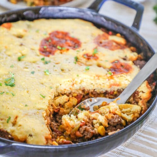 A spoon scoops out a serving of cowboy casserole from a cast-iron skillet
