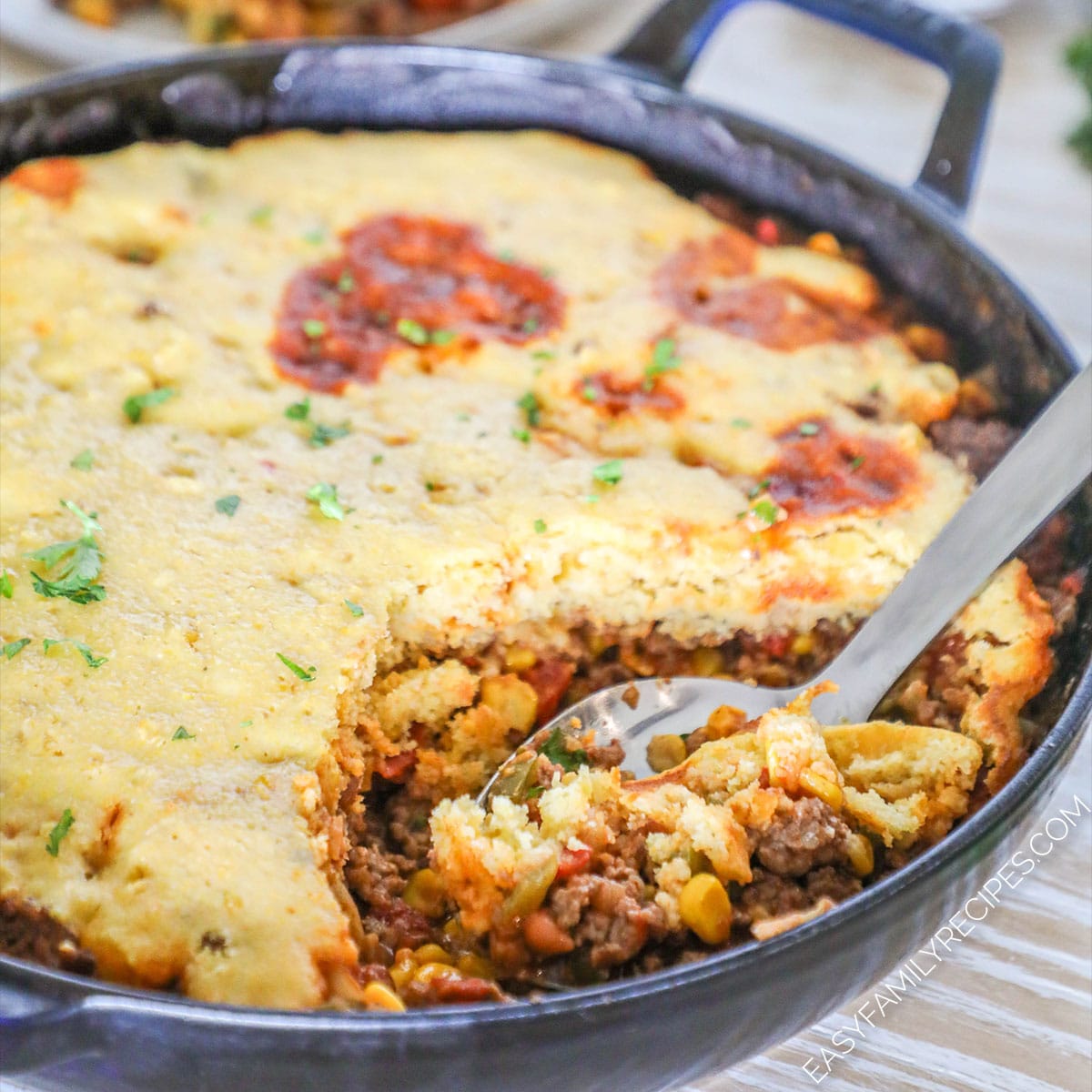 A spoon scoops out a serving of cowboy casserole from a cast-iron skillet