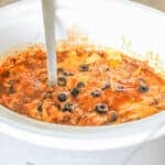 side view of a crockpot of finished beef enchilada casserole.