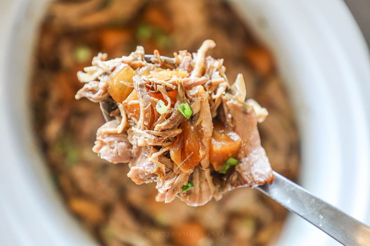 Close up shot of a portion of pineapple pork on a serving spoon hovering over the crockpot.