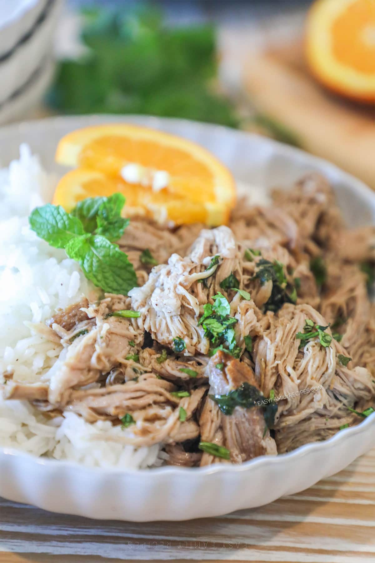 Crockpot Cuban Style Mojo Pork in a white bowl with rice plus mint and orange garnish